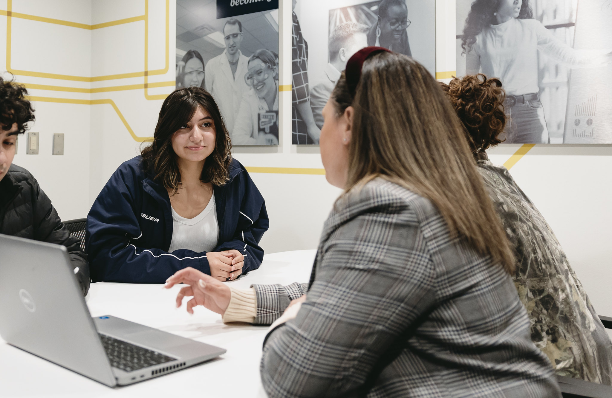 Student listens during a small group meeting around a table with a laptop open.