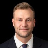 Man in a dark suit and tie poses for a professional headshot.