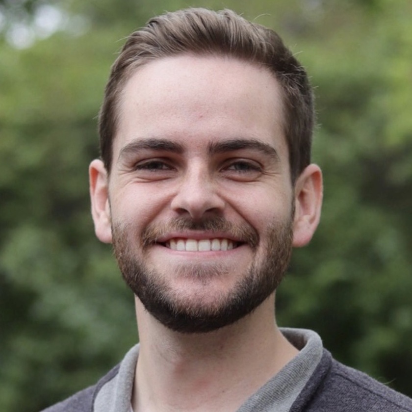 Jacob McCullough smiles outdoors in a gray collared shirt.