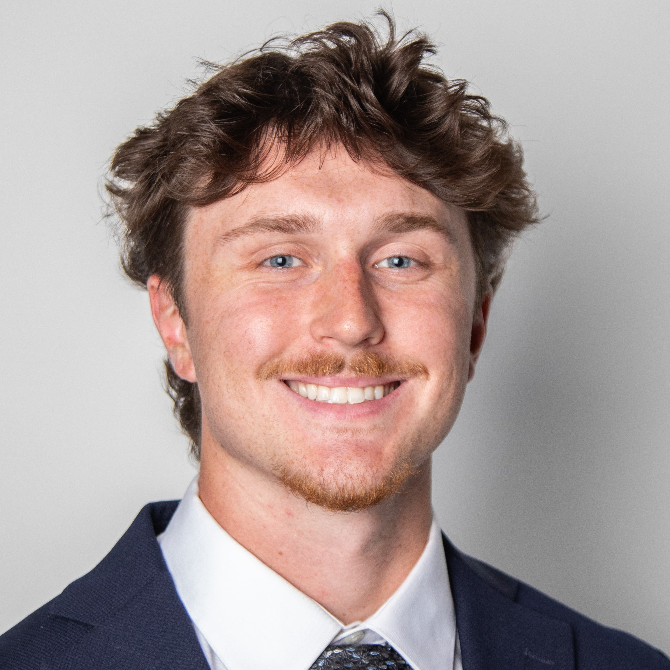 Wes Myers smiles in a navy suit and patterned tie against a light background.